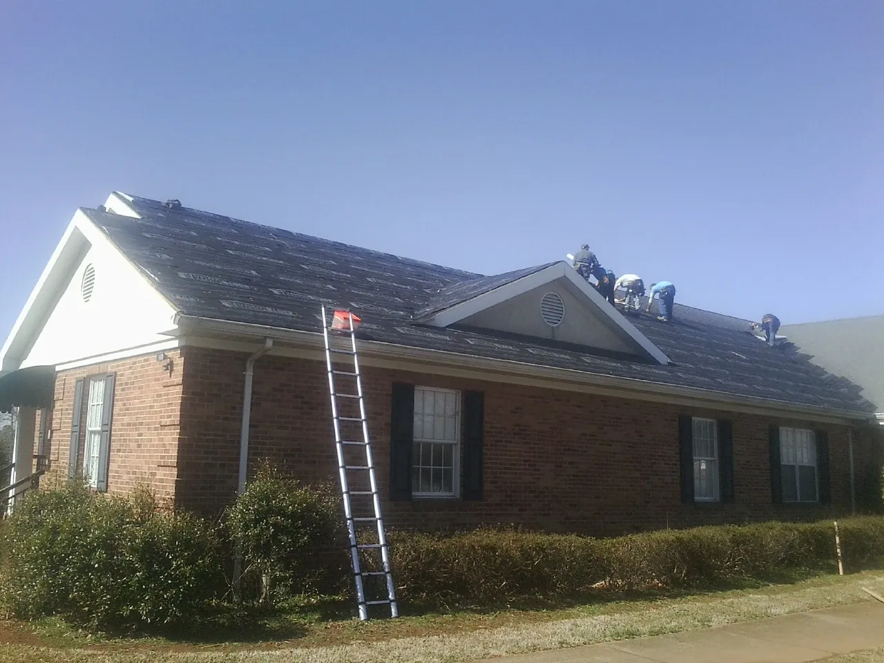 Crew tearing shingles off a brick ranch roof with a ladder set — Emergency Roof Repair work by our crew in Benton