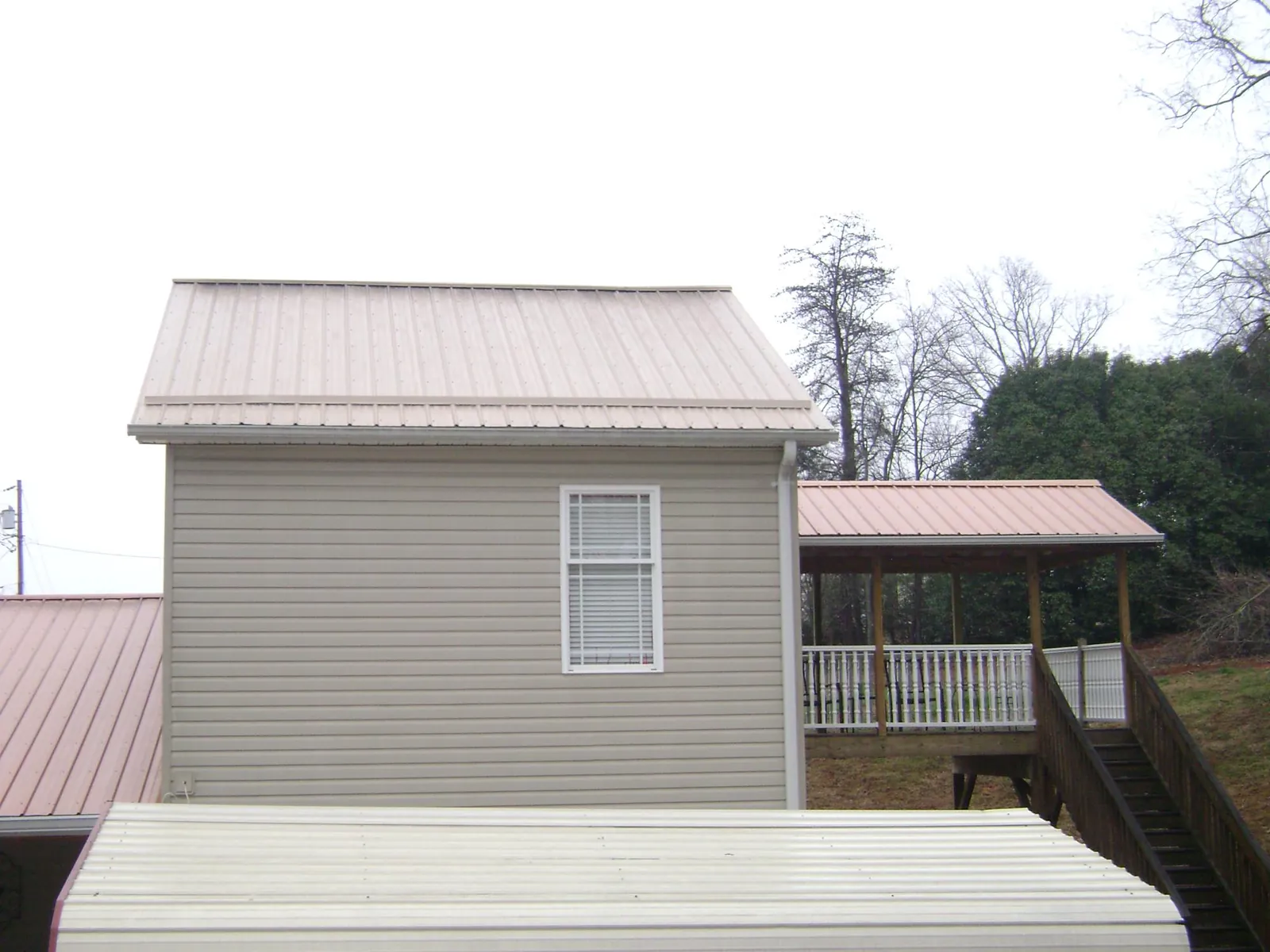 Tan metal roofs on a two story addition and attached porch, from a Roof Replacement job in Benton